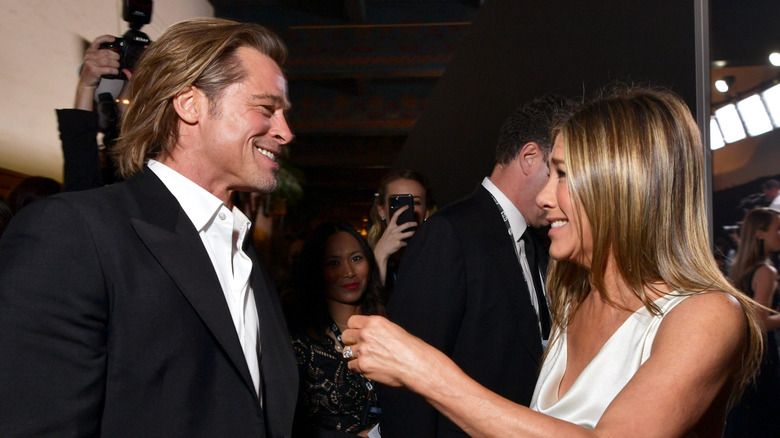 Brad Pitt wearing a suit and holding his SAG award holding Jennifer Aniston's hand, who's wearing a white dress.