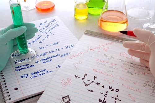 Scientist holding a pen over chemistry formulas on hand written notepads for assay notes comparison with a laboratory technician showing a scientific cylinder filled with green liquid during an experiment in a science research lab. Experiment stock images, royalty-free photos and pictures