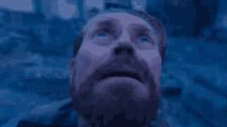 a man with a beard is looking up at the sky in a blue light .