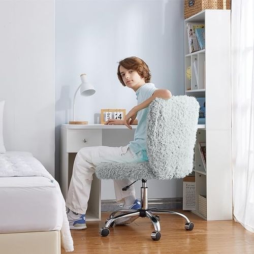 Teen seated on a fluffy swivel chair at a desk with books, a lamp, and a calendar, in a cozy bedroom setting