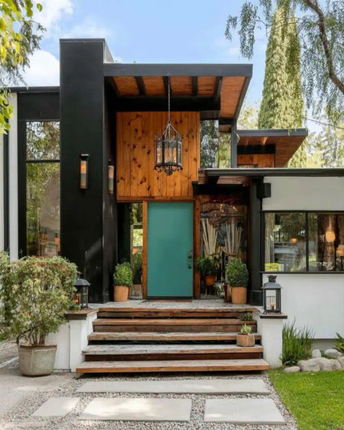 A mid century modern home exterior with a high-contrast entry, featuring a teal door, black-painted structure, and knotty wood siding.