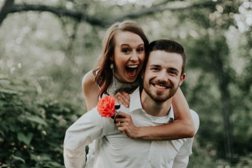 A couple having a piggyback ride while taking funny wedding poses.