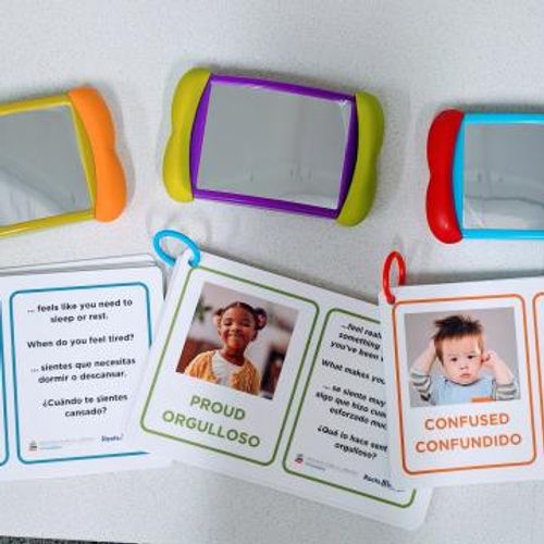 A series of booklets with babies making faces and small mirrors is displayed against a white backdrop.