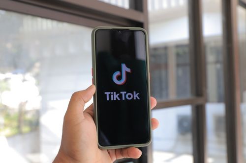 Free A hand holds a smartphone displaying the TikTok app in an indoor setting. Stock Photo