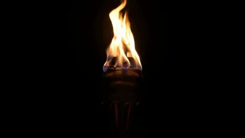 A single flaming torch burns brightly with a flickering fire, isolated against a pitch black background at night