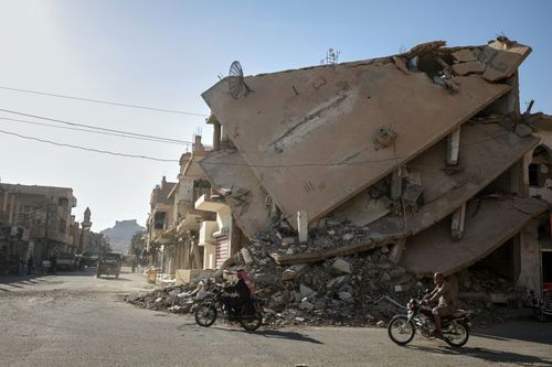 Locals ride a motorcycle along a war-damaged street in Palmyra, Syria