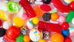 Colorful candy background, candy closeup. Sugar concept for sweets and treats, unhealthy eating junk food, or sugar rush indulgence in childhood nostalgia. Candies include red licorice, gummy candy, chocolate nonpareils, gumballs, salt water taffy, peppermint candy, and jawbreaker candy. This image could also represent artificial flavor and artificial color food. Multi-colored large group of objects, candy on white background. Part of a series.