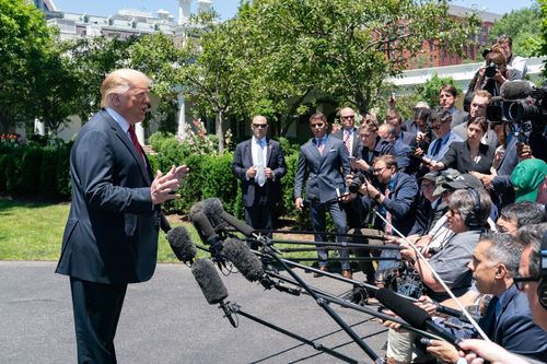 Trump at the South Lawn driveway of the White House facing a crowd of reporters with cameras and boom microphones
