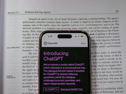 Free Smartphone showing OpenAI ChatGPT in focus, on top of an open book, highlighting technology and learning. Stock Photo