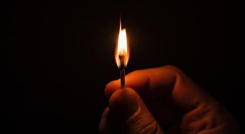Hand holding a burning matchstick against a dark background photo