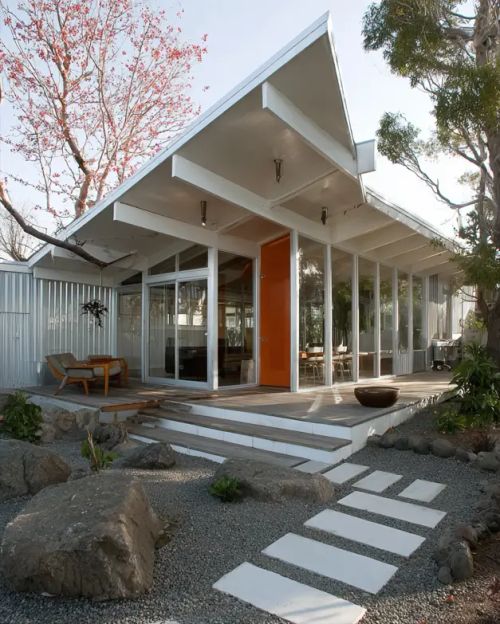 A mid century modern house exterior with a pitched roof, corrugated metal siding, and an orange front door.
