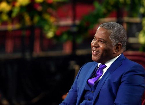 Robert F. Smith wears a blue suit as he sits in a chair smiling