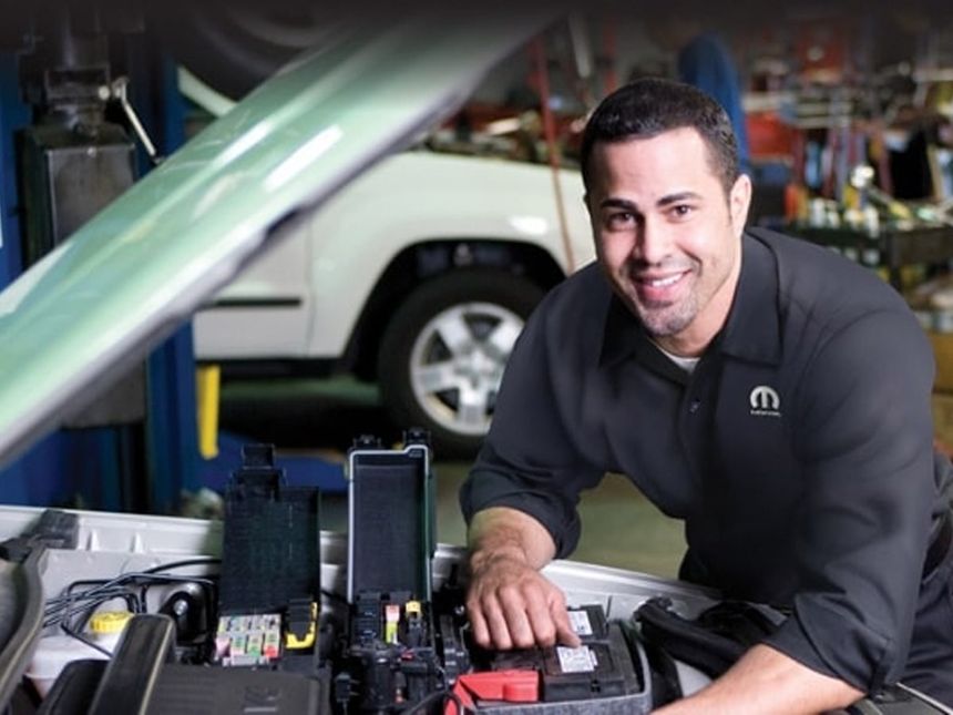 Technician inspecting a vehicle battery during winter maintenance at a Southern California CDJR service center.