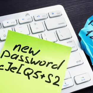 A strong password written on a yellow Post-it note sitting on top of an Apple keyboard.