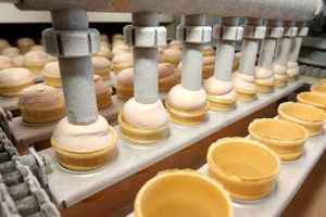 Rows of ice cream cones being filled with ice cream by a machine in a factory production line.