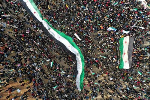 An aerial picture shows Syrians waving the national flag during a gathering in the rebel-held city of Idlib on March 15, 2021, as they mark 10 years since the nationwide anti-government protests that sparked the country's devastating civil war.