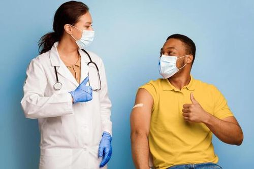 Covid-19 Vaccination. Vaccinated Black Man And Medical Worker Gesturing Thumbs-Up After Successful Coronavirus Immunization Posing Wearing Face Masks In Studio Over Blue Background. photo