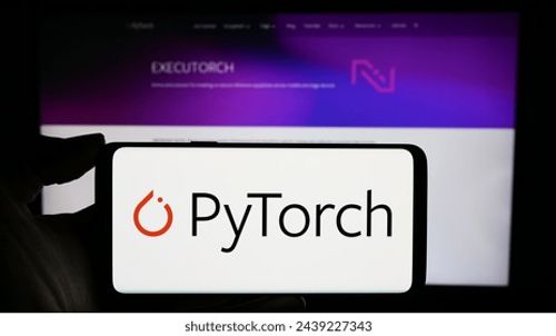 Stuttgart, Germany - 03-12-2024: Person holding cellphone with logo of machine learning library PyTorch in front of webpage. Focus on phone display. Unmodified photo. Editorial Stock Photo