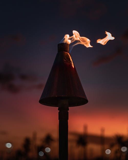 Free Silhouetted tiki torch against a vibrant Hawaiian sunset, capturing a fiery flame. Stock Photo