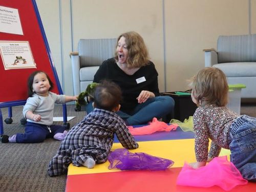 A librarian sits on the floor with a hand puppet on surrounded by three babies