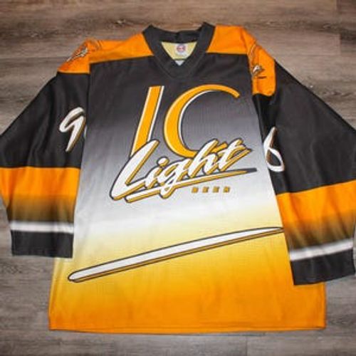 May include: A black, white, and yellow hockey jersey with the text "LC Light Beer" across the front. The jersey has a V-neck collar and long sleeves with black and yellow stripes. The jersey is made of a shiny material.