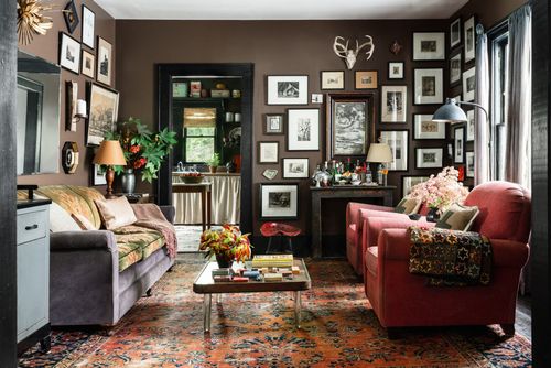 living room with collection of mismatched artwork hung on the wall brown wall with red chairs