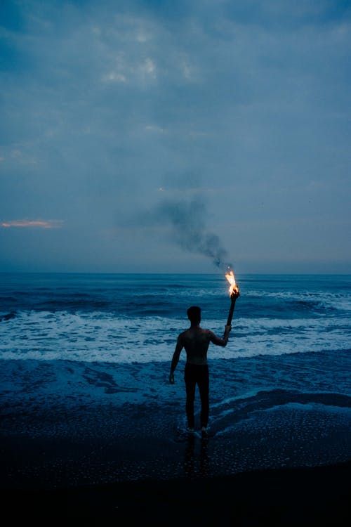 Free Silhouette of a man holding a torch by the sea during dawn at Playa Chachalacas, Mexico. Stock Photo