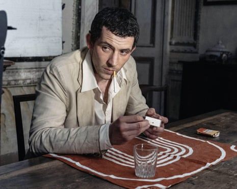 Josh O’Connor in La Chimera.sitting at a wooden table in a beige suit