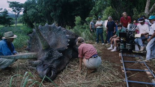 Sam Neil, Laura Dern and the crew gathered around a triceratops about to give birth.
