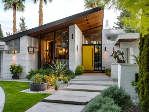 A stunning mid century modern house exterior featuring a bright yellow front door, white painted brick, a dramatic sloped roof, and desert-style landscaping.