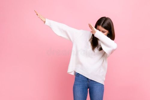 Woman with dark hair showing popular internet meme pose, celebrating success victory, dabbing trends, wearing white casual style sweater. Indoor studio shot on pink background. Meme pose stock images, royalty-free photos and pictures