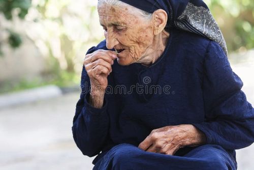 Elderly woman in blue dress eating cherry outdoors. Elderly people eating stock images, royalty-free photos and pictures