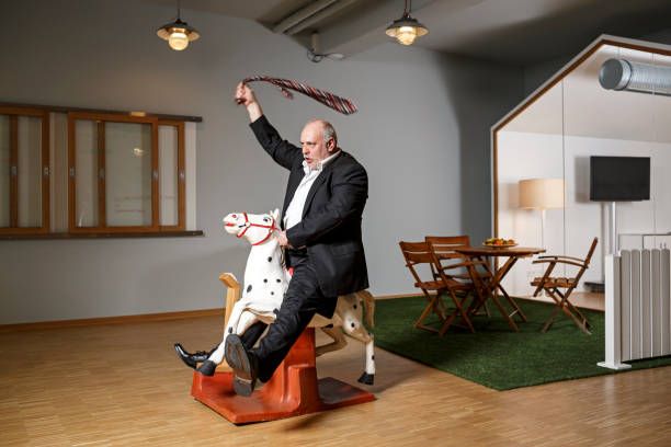 businessman on rocking horse pretending to ride - ridiculo fotografías e imágenes de stock