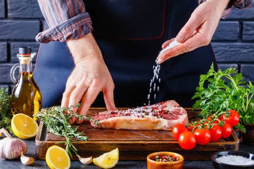man cooking beefsteak on a kitchen, close-up male chef is sprinkling salt over a porterhouse beef steak on restaurant kitchen. man cooking beefsteak salty foods stock pictures, royalty-free photos & images