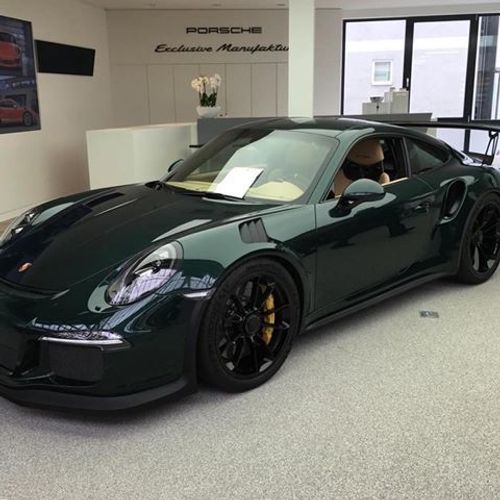 a dark green sports car is parked in a showroom with two people sitting inside
