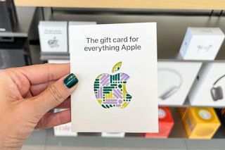 An Apple gift card held outlay hand in front of other Apple products.