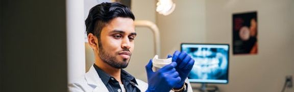 Man in lab coat and blue medical gloves inspecting a tooth mold