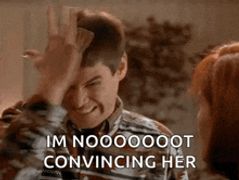 a man is making a funny face while holding his hand to his forehead and talking to a woman .