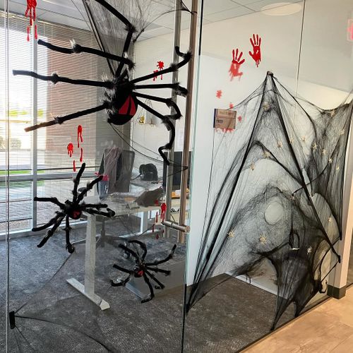 Office Halloween decor features large fake spiders, black webbing, and red handprint stickers on glass walls and doors—perfect inspiration for your own office Halloween decoration ideas.