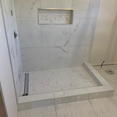 a bathroom with white marble tile and hexagonal flooring, including a walk in shower
