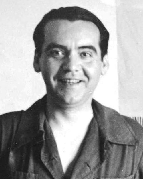 Federico García Lorca smiling, standing in front of a theatre poster