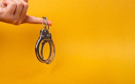 Female hand holding handcuff with copy space on yellow background illegal arrest