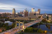 This image presents a panoramic view of Minneapolis during twilight, capturing the city skyline and a prominent bridge over a river. The scene is well-framed with the bridge leading the eye toward the downtown area, creating a sense of depth. The lighting is favorable, with warm artificial lights from buildings and the bridge contrasting against the cool blue and purple hues of the evening sky, creating a visually appealing and atmospheric mood. The composition is balanced, with the horizon level and no noticeable tilting, and the framing includes both natural and urban elements effectively. The skyline features distinctive buildings, including the IDS Center and other recognizable high-rises, which contribute to the city's recognizability. There are no significant distractions such as poles or clutter; vehicles on the bridge add a sense of life without overwhelming the scene. The technical quality is high, with sharp details, minimal noise, and no visible motion blur or focus issues. There are no borders, text overlays, or unwanted elements like people in the foreground. The overall beauty of the image is strong, conveying a vibrant and inviting urban landscape. This makes it highly suitable for a travel guide cover, as it effectively captures the essence of Minneapolis in an aesthetically pleasing manner.