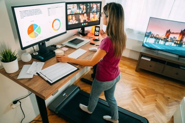 Woman at standing desk home office talking on business video call Woman working from home at standing desk is walking on under desk treadmill home office stock pictures, royalty-free photos & images