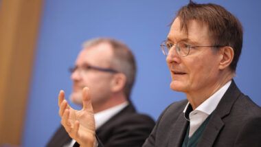 Bundesgesundheitsminister Karl Lauterbach (SPD) gestikuliert bei einer Pressekonferenz vor blauem Hintergrund