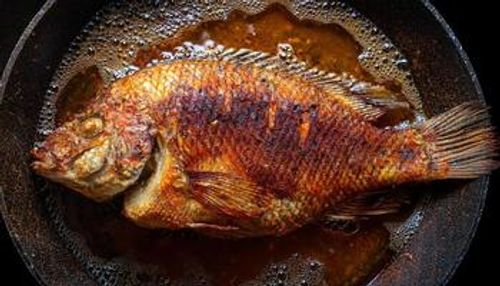 top view of a whole tilapia fish frying in sizzling hot oil with golden crust and crispy texture details photo