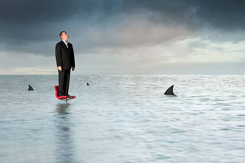 man trapped in the middle of a sea of sharks on chair - difficult-situations stock pictures, royalty-free photos & images