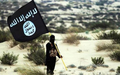 Islamic State/Iraq/Syria: A masked Islamic State soldier poses holding the ISIL banner somewhere in the deserts of Iraq or Syria. ISIL publicity...