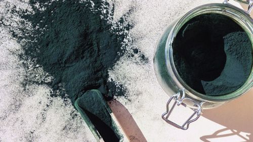 Powdered spirulina in a jar and on a table.-2