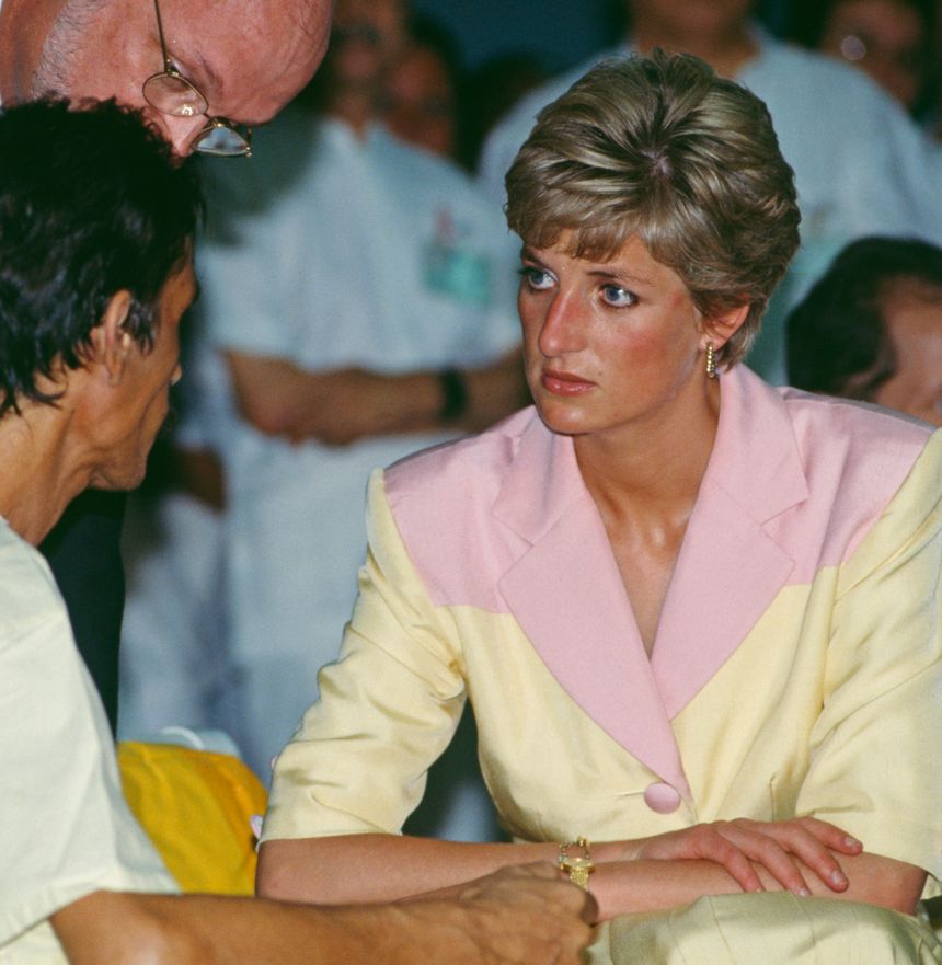 Princess Diana in a yellow and pink blazer talking to a man in a hospital gown